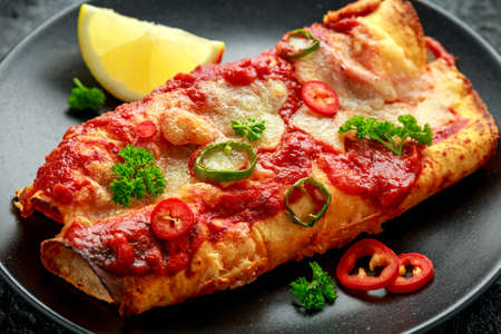 Baked Chicken fillets enchiladas with courgette, salsa sauce and cheese served with lemon wedges and chiliesの写真素材