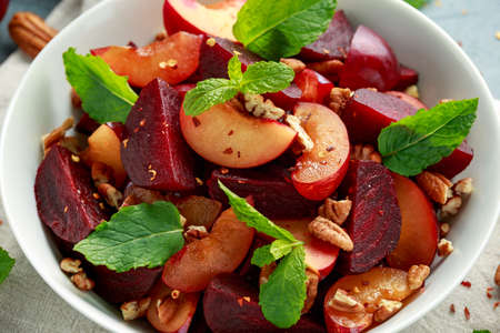 Vegan Plum, beet salad with pecan nuts, mint and herbs in white bowl. healthy summer food.