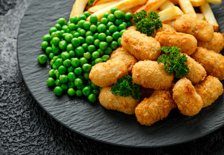 Crispy Battered scampi nuggets served on slate plate with potato chips and green peasの写真素材