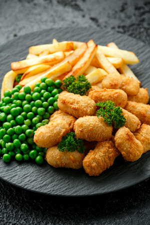 Crispy Battered scampi nuggets served on slate plate with potato chips and green peasの写真素材