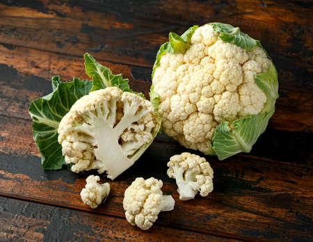 Raw Cauliflower head harvest with green leaves on dark wooden background