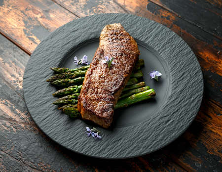 Grilled Sirloin beef steak on fried asparagus served on black slate plate with rosemary flowers.の写真素材