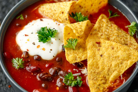 Mexican Chilli bean soup with yogurt, cheese and tortilla chips in black bowlの写真素材