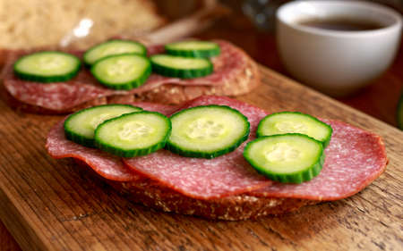 Rye Bread open sandwich with salami, cucumber on wooden board.の写真素材
