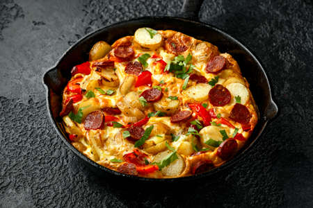 Frittata made of eggs, potato, chorizo, red bell pepper and greens in iron cast panの写真素材