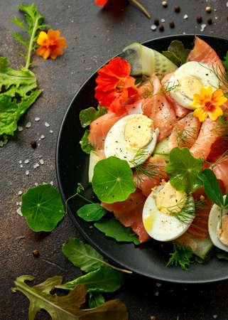 Smoked salmon and cucumber salad with nasturtium leaves and edible flowers. healthy food.