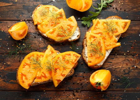 Vegetarian Sourdough toasts with soft cheese and orange beefsteak tomatoes on rustic wooden background.の写真素材
