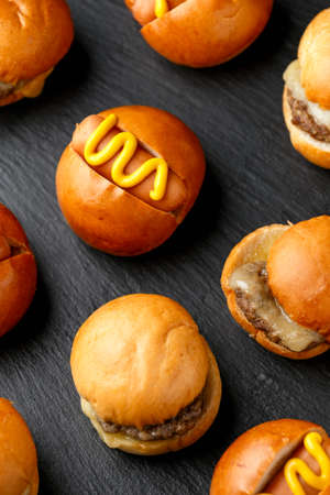 Mini hamburgers, burger and hot dogs with yellow mustard on black slate boardの写真素材