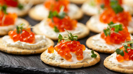 Salmon caviar and soft cheese savory crackers with sesame and poppy seeds served on black slate...