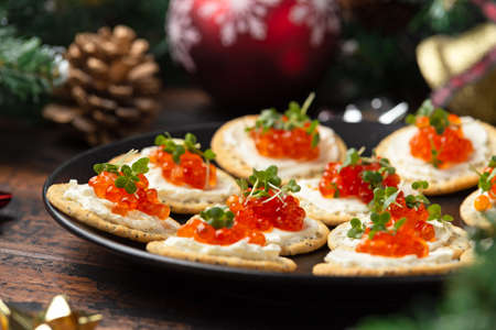 Salmon caviar and soft cheese savory crackers with decoration, gifts, green tree branch on wooden rustic table.の写真素材