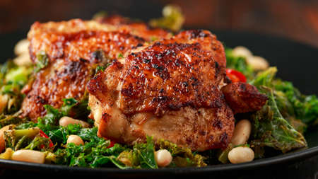 Roasted chicken thighs with kale and cannellini beans served with chili peppersの写真素材