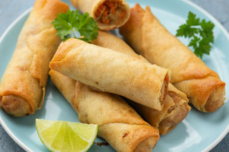 Fried spring rolls with sweet chili sauce and lime on plate.
