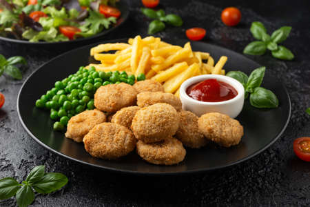 Fried crispy chicken nuggets with ketchup, french fries and green peas in black plateの写真素材