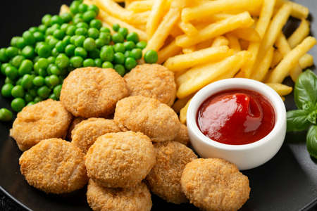 Fried crispy chicken nuggets with ketchup, french fries and green peas in black plateの写真素材