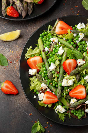 Asparagus and Strawberry Salad with vegetables, green peas and feta cheese in black plate. healthy food.の写真素材