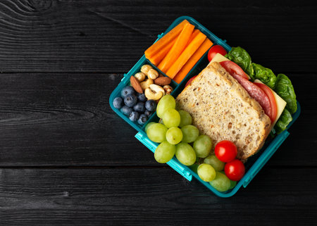 Healthy school, work lunch box with sandwiches and fresh vegetables, nuts and fruits on wooden tableの写真素材