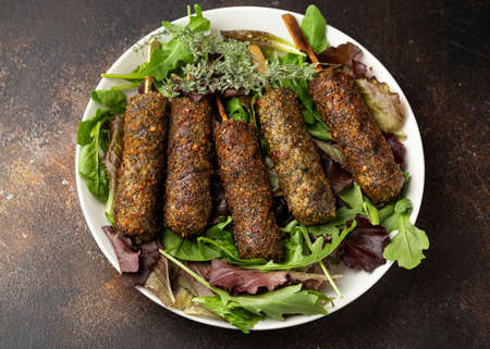 Homemade Kofta kebabs on skewers with vegetables on white plateの写真素材
