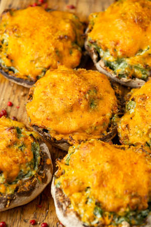 Soft cheese and spinach stuffed mushrooms with cheesy crust served on rustic wooden board, vegetarian food.の写真素材