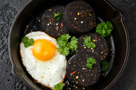 Cooked Black Pudding with egg, herbs and parsley on iron cast panの写真素材