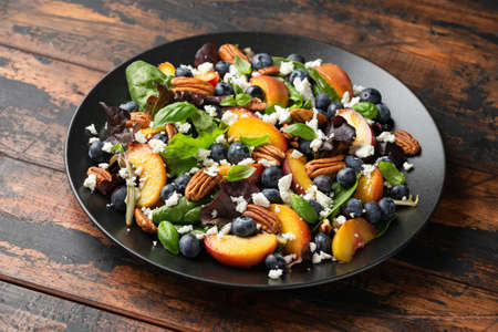 Peach, blueberry salad with vegetables, feta cheese and pecan nuts. Healthy summer food.の写真素材