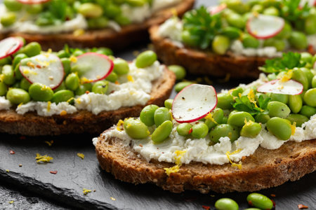 Soya bean and goats cheese sourdough bruschetta served with lemon zest and reddish on black slate boardの写真素材