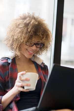 Beautiful girl working on her laptop while drinking coffeeの写真素材