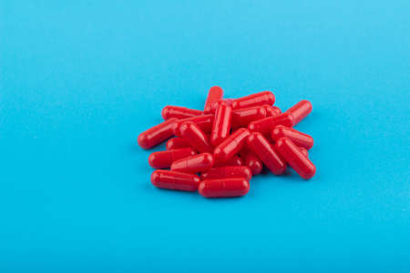 Heap of red pills (capsules) on a blue background, close-up