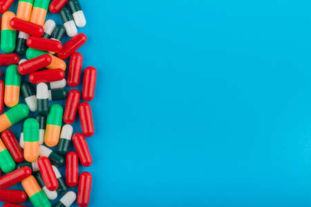 A heap of mixed colored pills on a blue background with copy space for textの写真素材