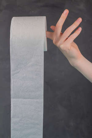 On the finger of a woman's hand holding a roll of toilet paper on a gray background, close-upの写真素材