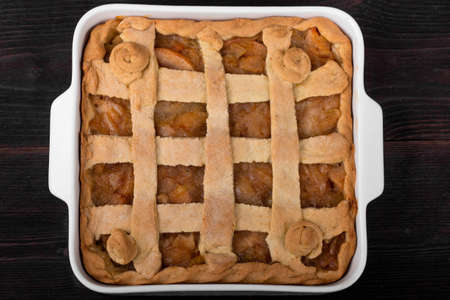 Apple pie in a white square ceramic baking sheet on a dark wooden background