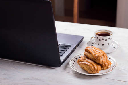 Profiteroles with cream with a Cup of coffee and a laptop, Coffee break. White wooden tableの写真素材
