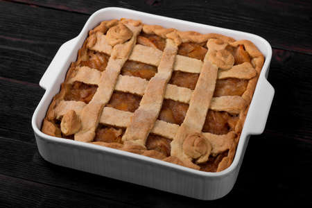 Apple pie in a white square ceramic baking sheet on a dark wooden background