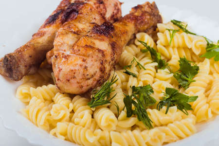 Grilled chicken drumstick and pasta on white plate, white background, close upの写真素材