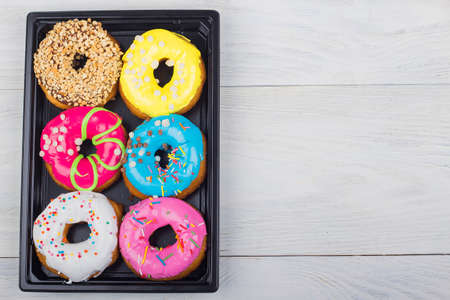 Colored donuts with glaze in a box on a white wooden background