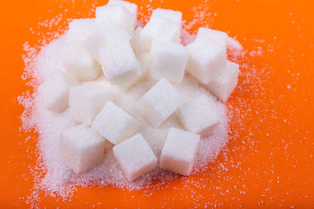 Cubes of white sugar and sugar on an orange background, close-up