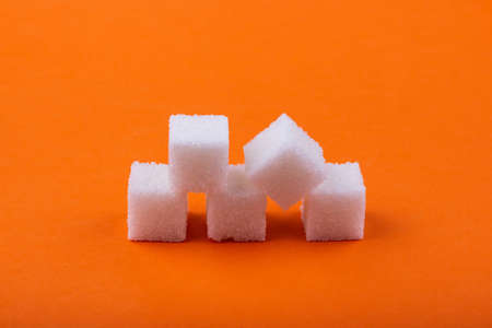 Cubes of white sugar on an orange background, close-up