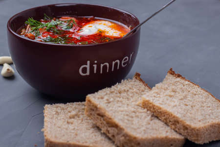 Ukraine borscht with sour cream, garlic and bread on gray background