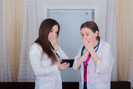 Two female doctors or nurses look at the tablet, one is shocked or very surprised, medicine concept.の写真素材