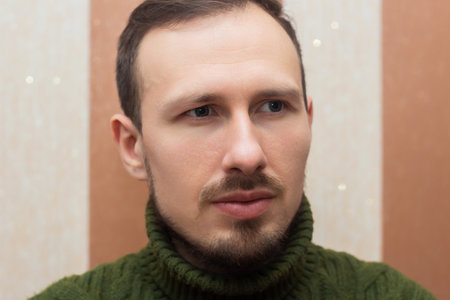 Male portrait, a man in a green sweater sitting on a sofa on a striped background