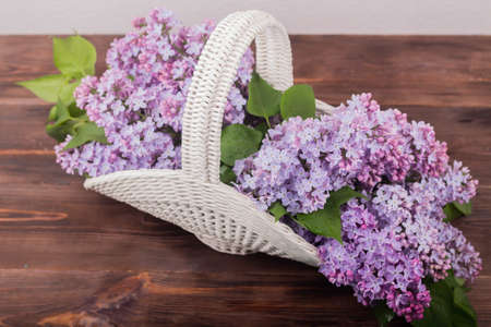 Beautiful white vintage wicker basket on a wooden table. Lilac flowers in a retro basket, home decorの写真素材
