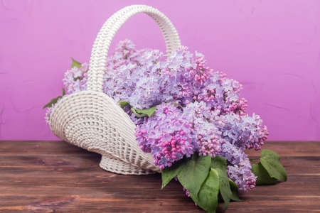 Beautiful white vintage wicker basket on a wooden table. Lilac flowers in a retro basket, home decorの写真素材