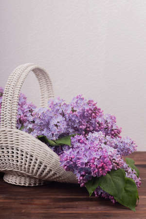 Beautiful white vintage wicker basket on a wooden table. Lilac flowers in a retro basket, home decorの写真素材