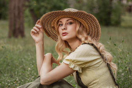Portrait of a beautiful woman with blonde hair in retro clothes with a hat in a park or garden