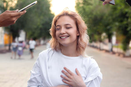 Portrait of a beautiful young laughing woman in white clothes, she is filmed on smartphones from...