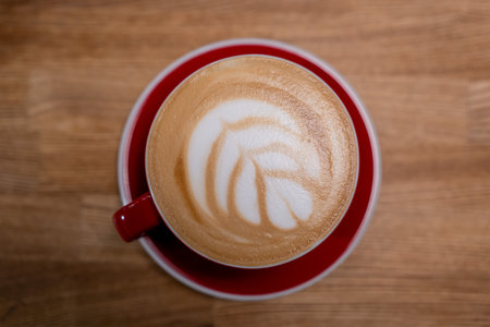 A cup of coffee, a cappuccino in a red mug on a wooden tableの写真素材