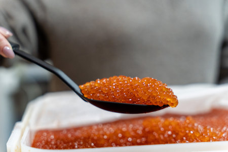 A spoon with red salmon caviar above a container of caviar, close-up