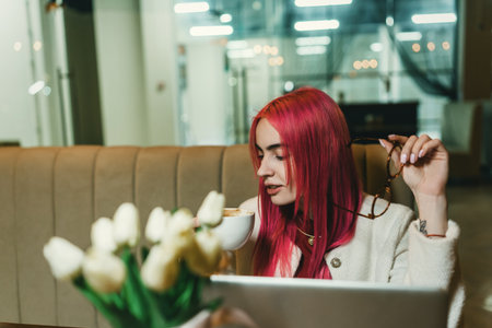 A girl with red hair is sitting with a laptop in a cafe