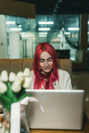 A woman with red hair is sitting with a laptop in a cafe