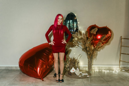 Sexy woman with red hair and red dress poses among inflatable heartsの写真素材
