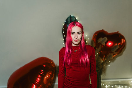 Sexy woman with red hair and red dress poses among inflatable heartsの写真素材